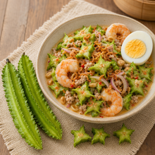 A bowl of shrimp and winged bean salad on a woven placemat over a wooden table, with two whole green winged beans and two sliced pieces placed beside the bowl.