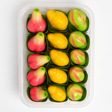 A clear plastic container holding 12 Thai fruit paste candies shaped like mangoes and lychees, arranged in two rows of six. The candies feature vibrant yellow, pink, and green colors, with some pieces showing a marbled pattern.